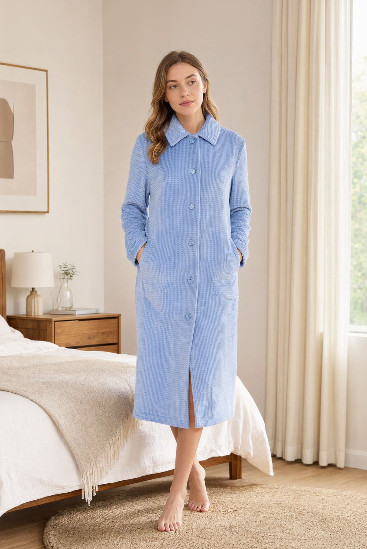 Mujer en un dormitorio con una bata larga azul de Lohe, modelo abotonado con diseño jacquard de cuadros en color acero.