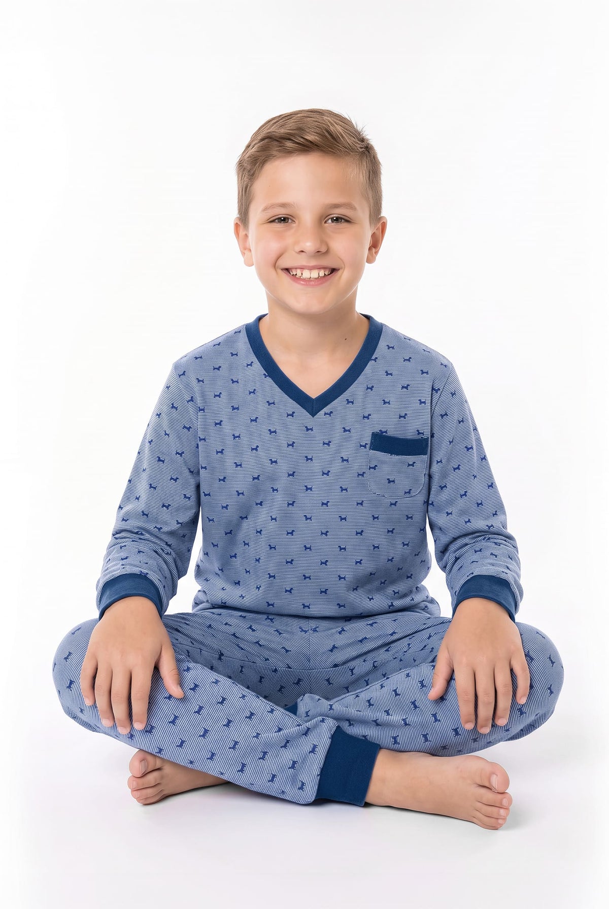 Niño sonriente sentado vestido con pijama de color azul con estampado de perritos y ribetes en azul oscuro