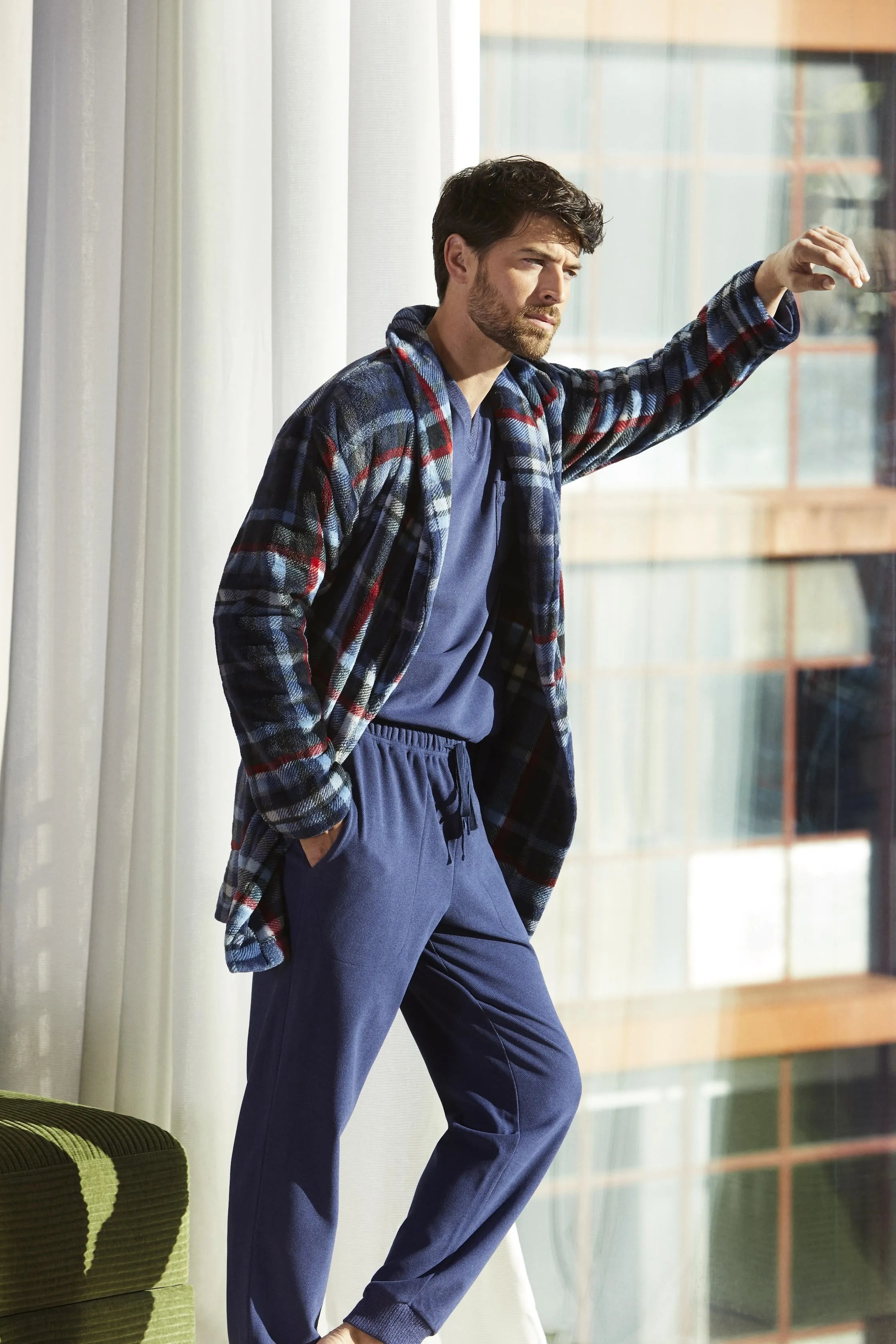 Hombre con bata de cuadros azules y pijama a juego junto a una ventana