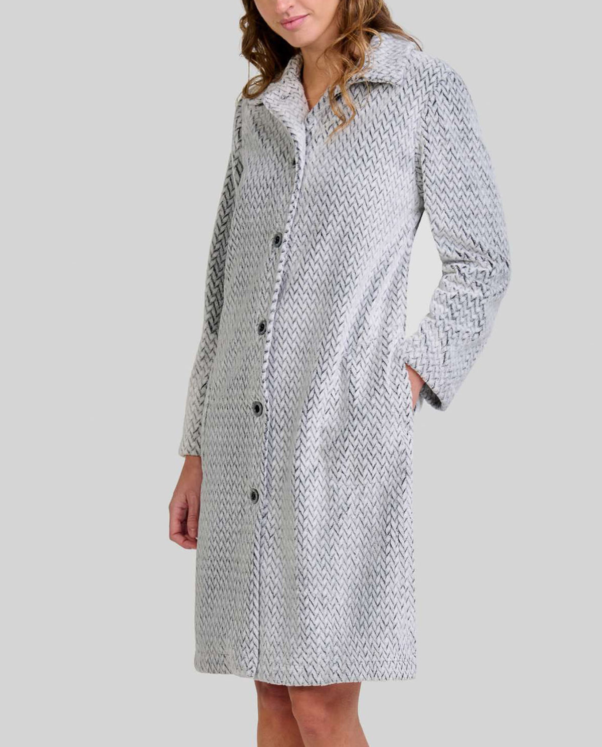 Mujer de pie descalza con bata larga gris claro y textura espiga, botones al frente y manos en los bolsillos