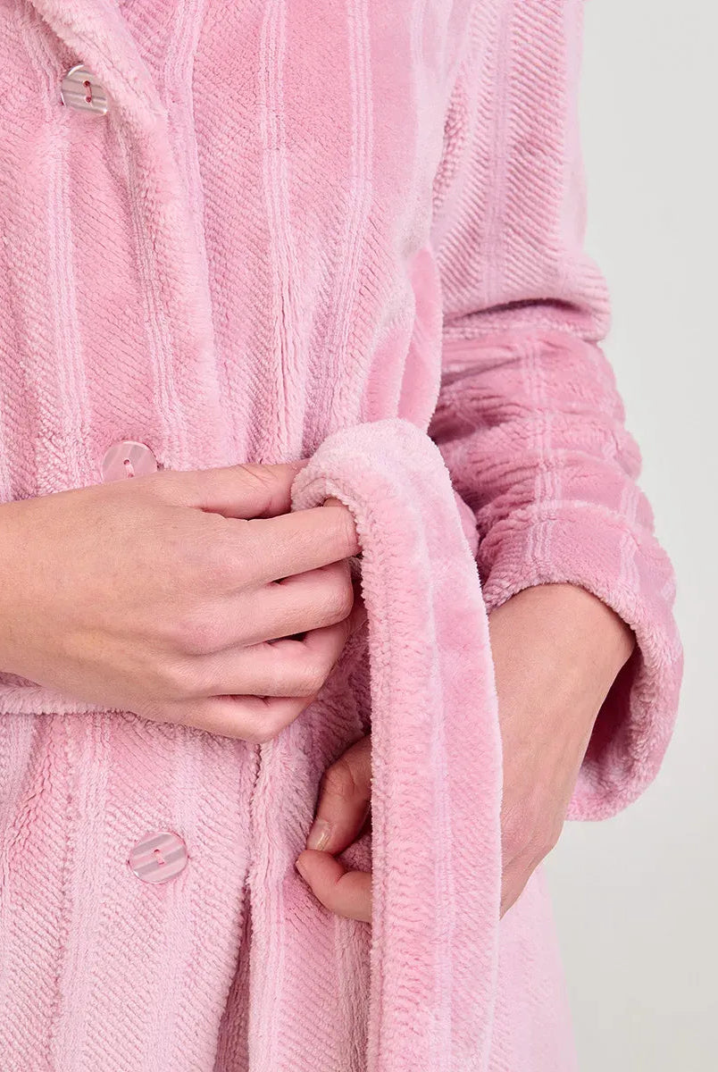 Mujer en camisón rosa claro y una bata Jacquard rosa a juego sentada en una mesa de madera junto a una ventana
