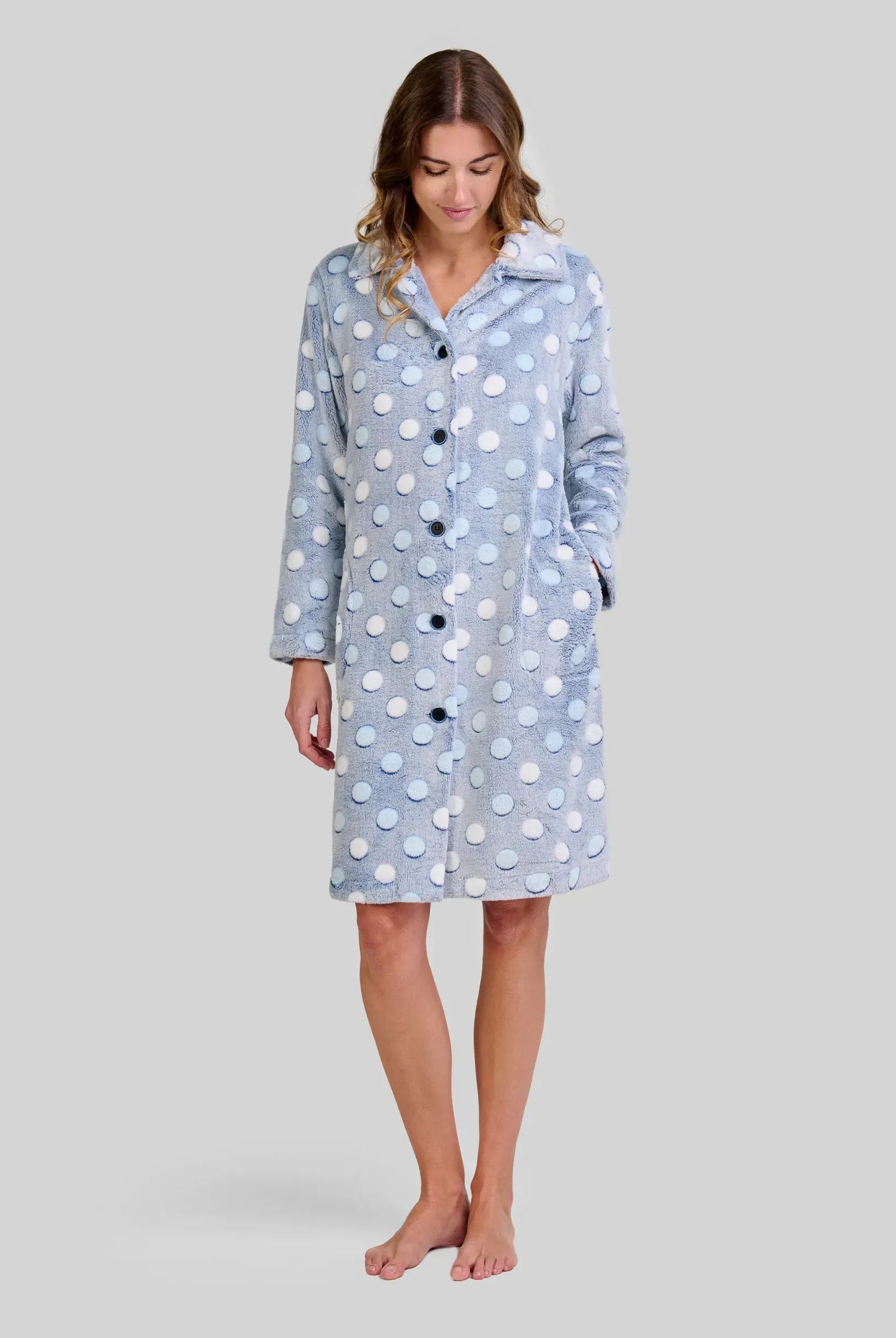 Mujer en bata celeste de lunares en relieve hasta la rodilla, manga larga y botones con bolsillos laterales.