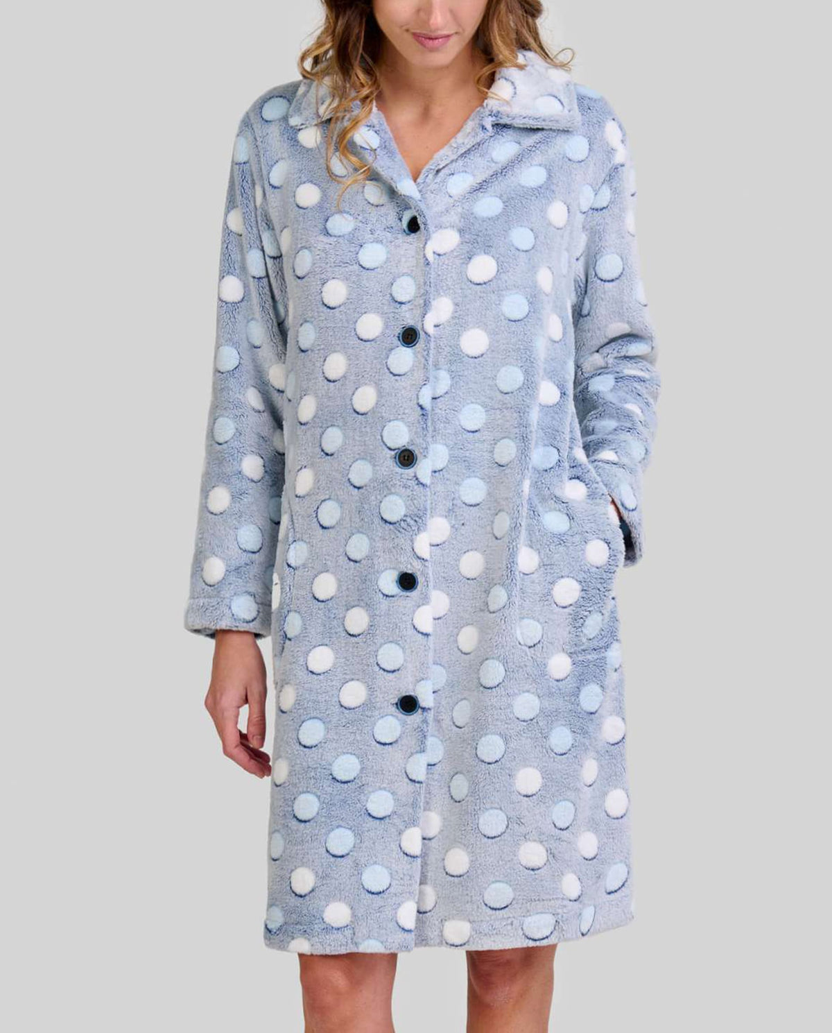 Mujer en bata celeste de lunares en relieve hasta la rodilla, manga larga y botones con bolsillos laterales.