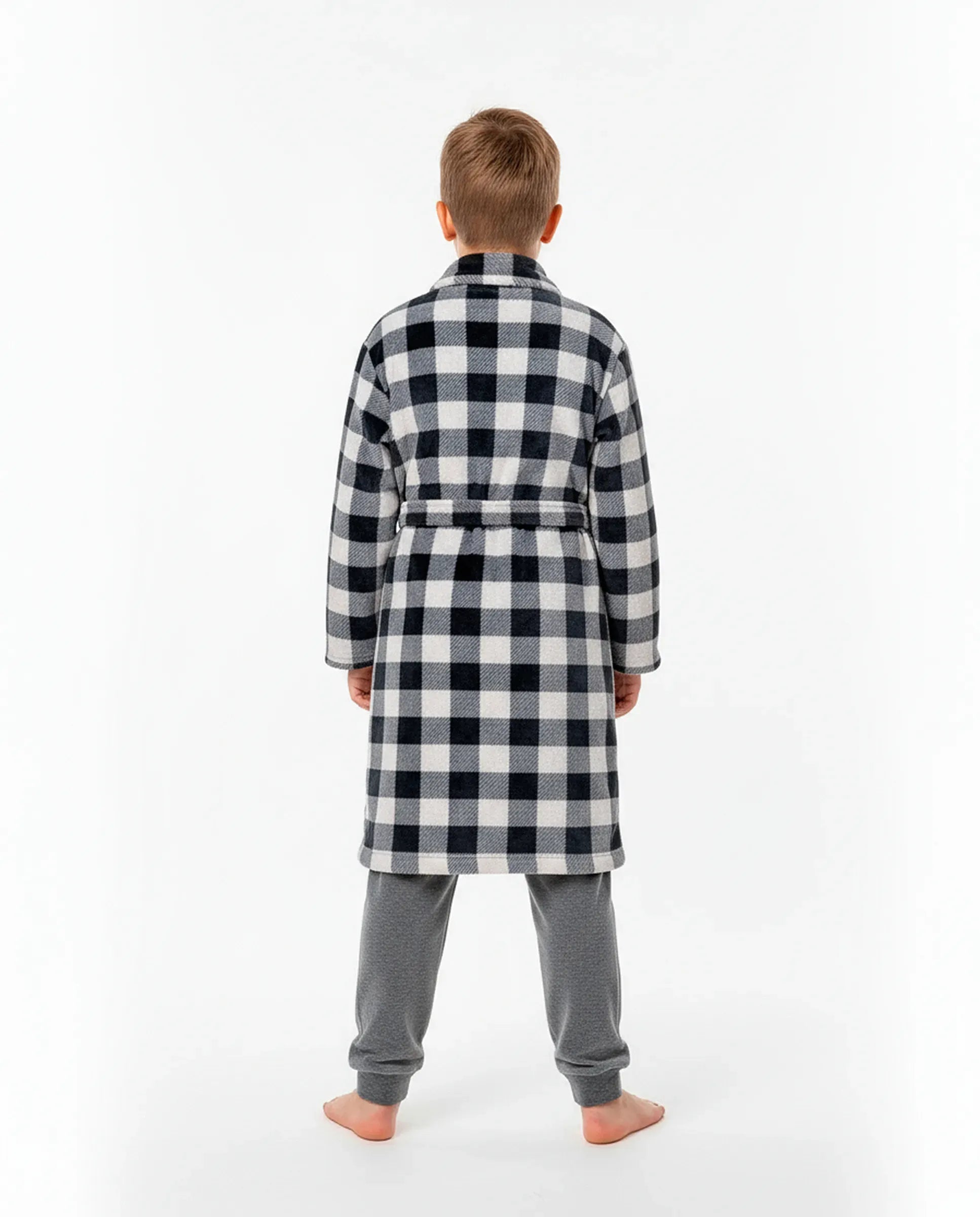 Niño de espaldas con cómoda bata a cuadros blanco y negro sobre pijama gris de terciopelo para invierno