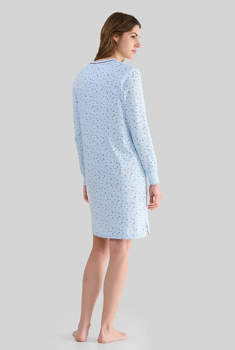 Mujer con top lencero celeste de manga larga, detalles de encaje blanco, botones, bolsillo en el pecho y lazo blanco decorativo.