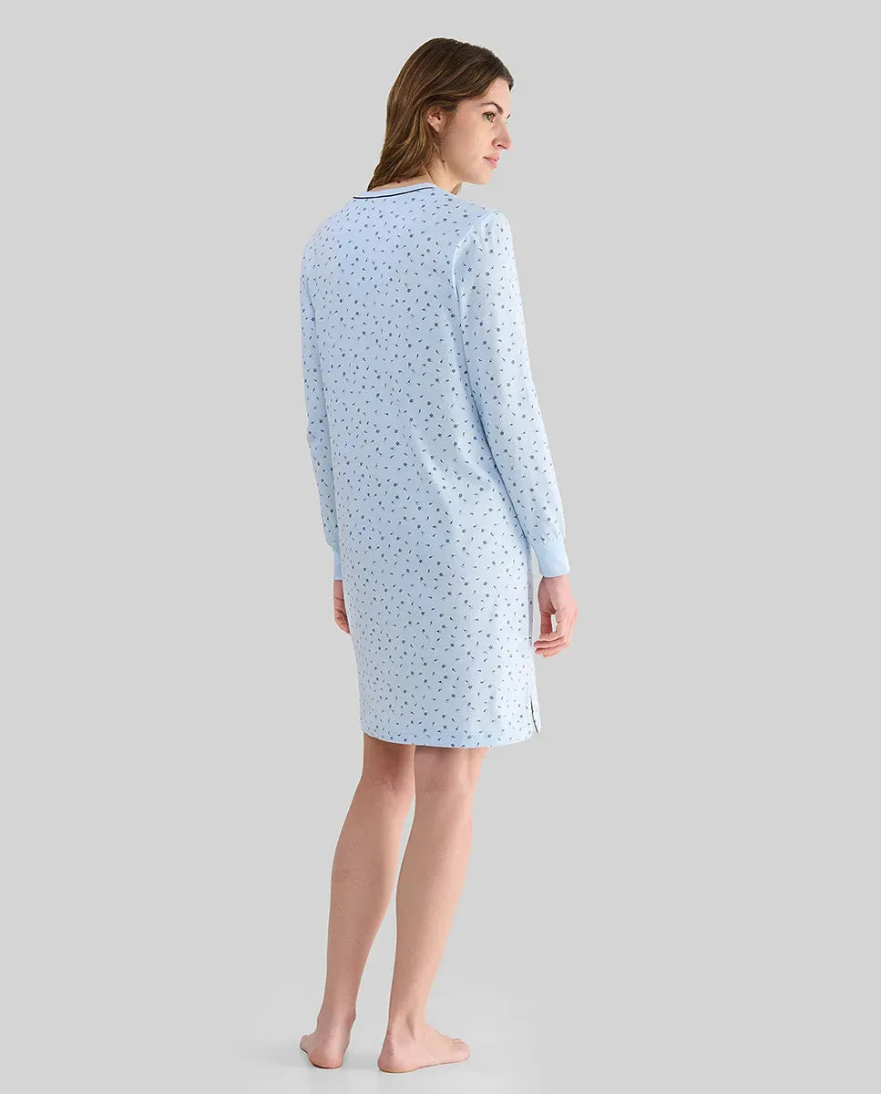 Mujer con top lencero celeste de manga larga, detalles de encaje blanco, botones, bolsillo en el pecho y lazo blanco decorativo.