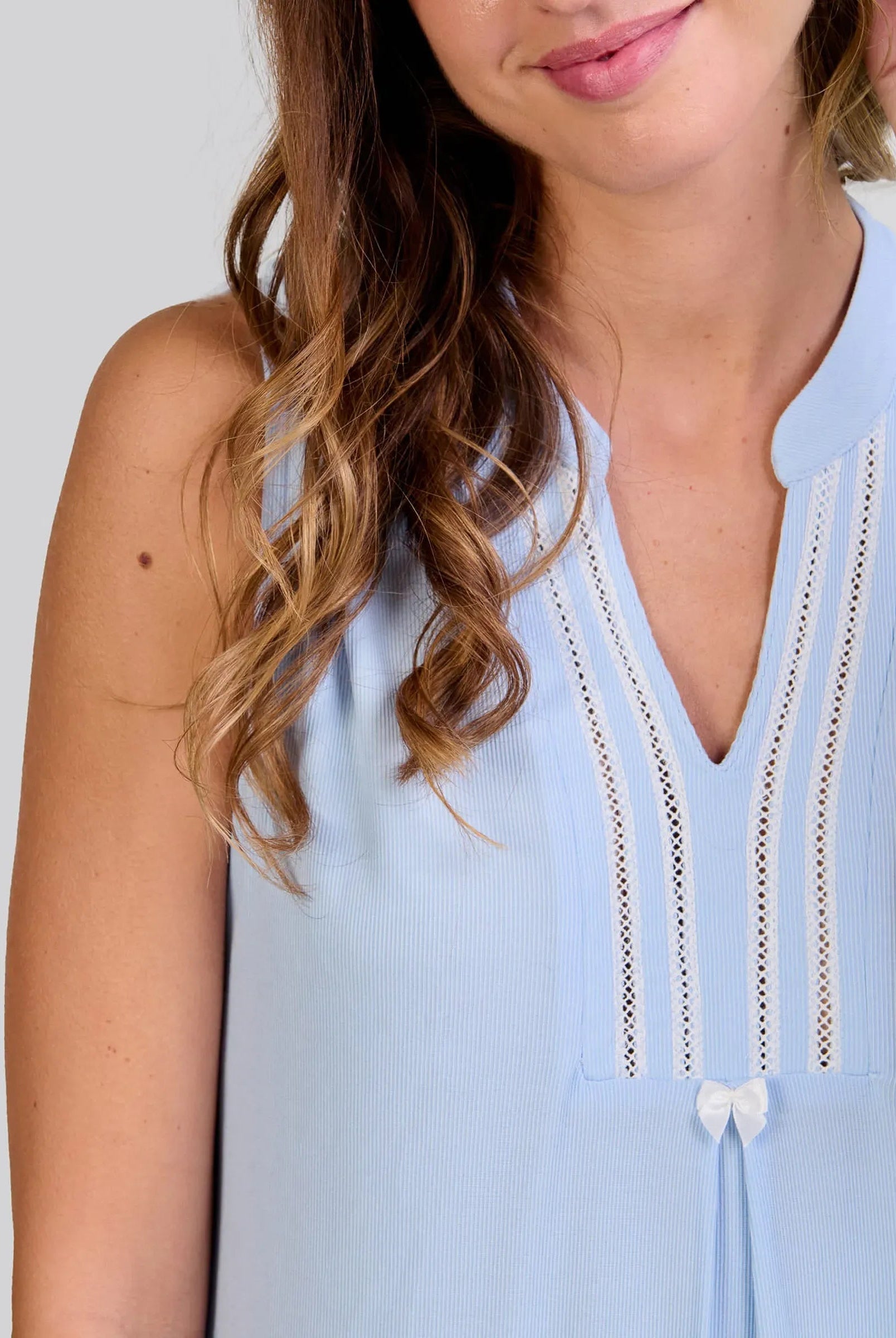 Detalle de camisón lencero sin mangas rosa claro con escote adornado con encaje y un pequeño lazo