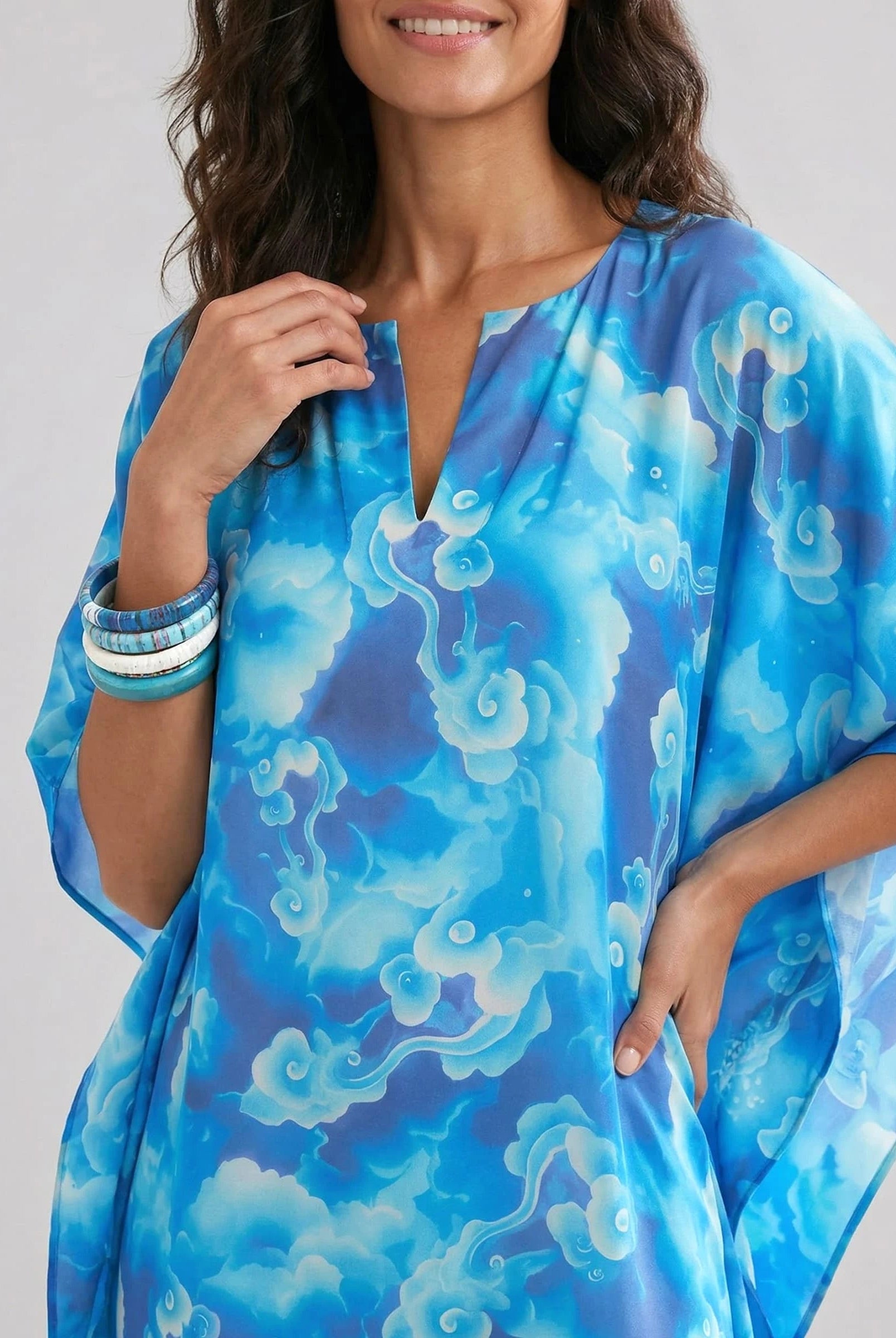 Vista detalle de mujer con kaftan azul de estampado abstracto, con pulseras en la muñeca.