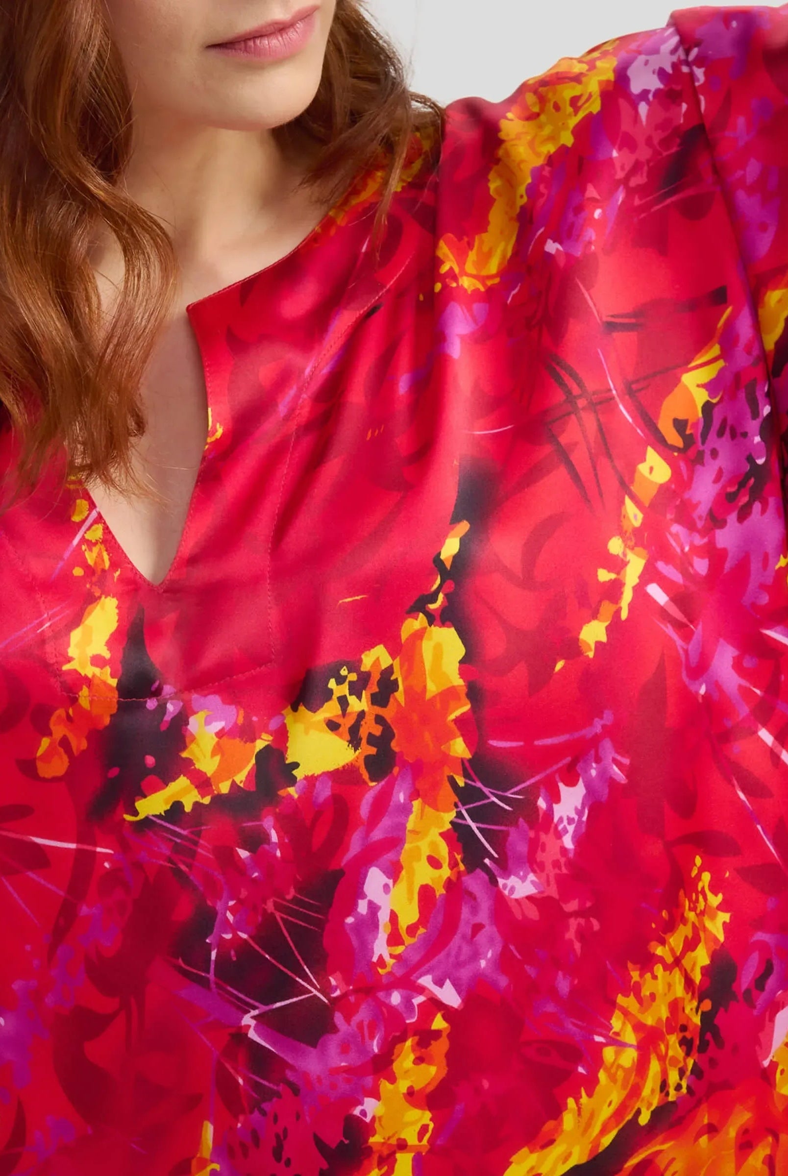 Mujer luciendo caftán de seda de color rojo con un llamativo estampado floral y detalles en amarillo y negro.