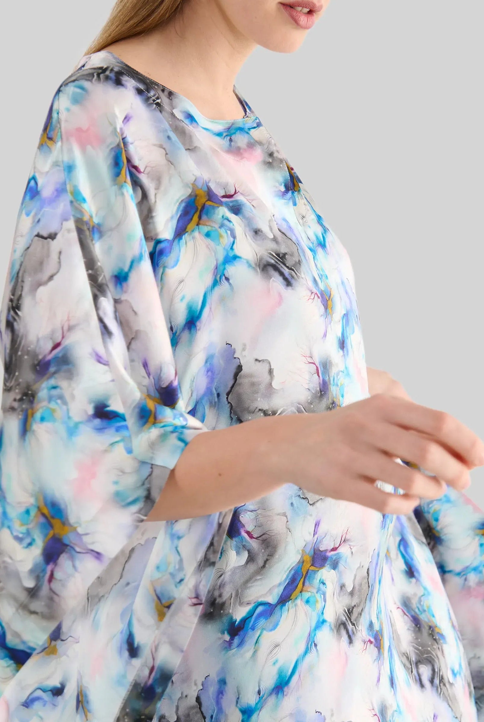 detalle de mujer luciendo un caftán fluido de estampado abstracto en tonalidades azul, rosa y gris con manga al codo