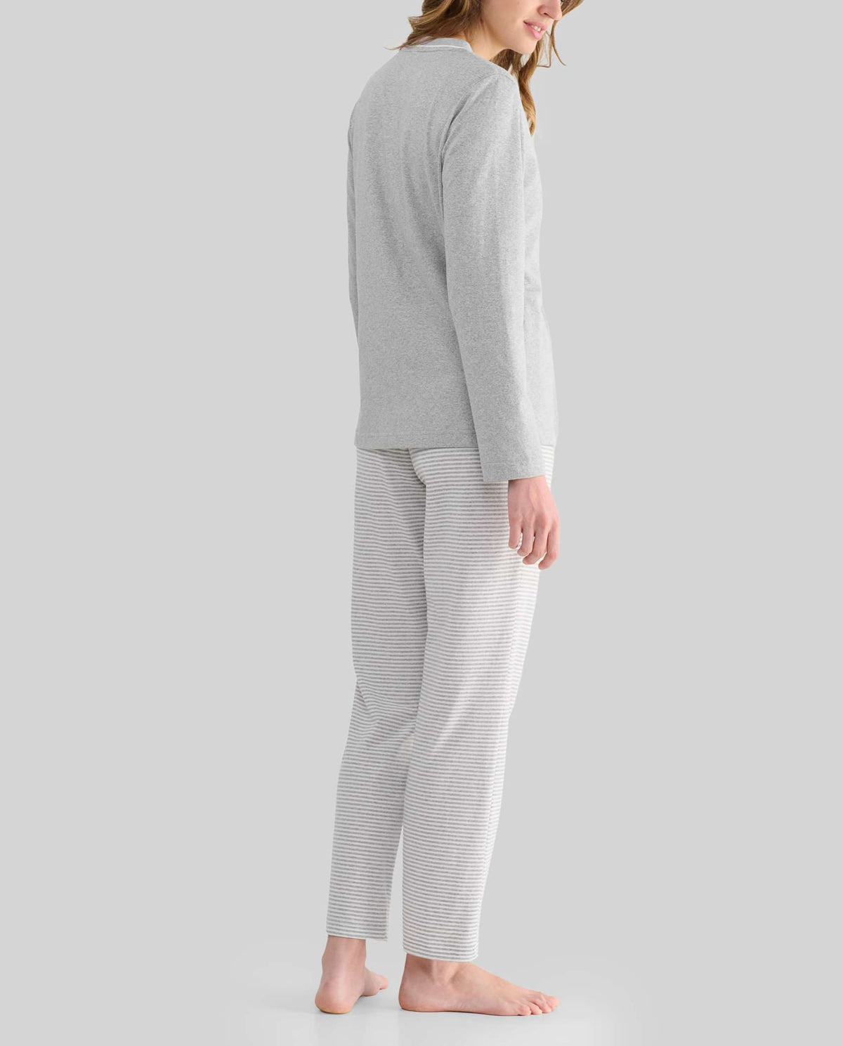 Mujer de perfil con pijama de invierno gris y pantalón de rayas a juego