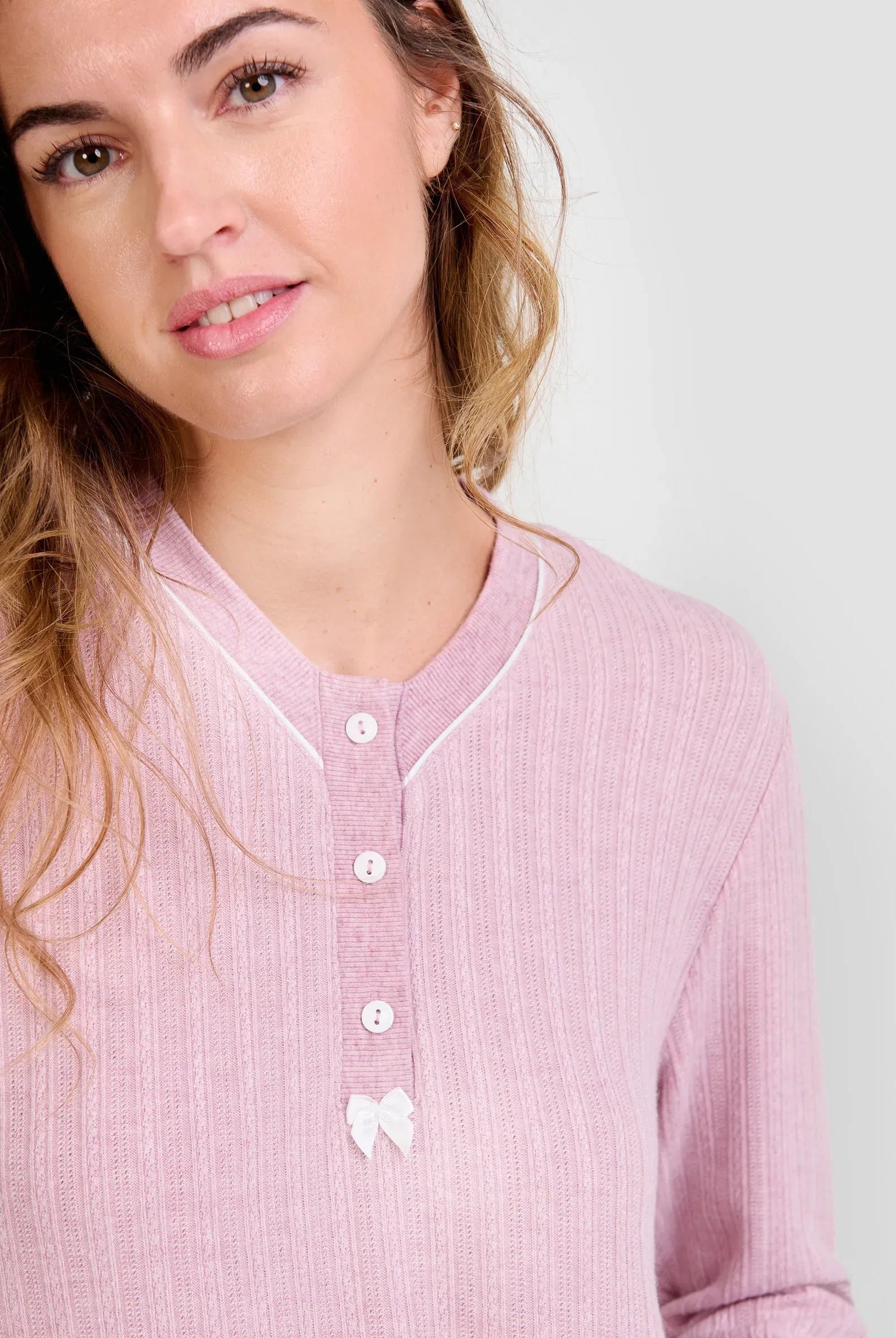 Mujer luce chaquetilla de pijama de invierno rosa de manga larga, cuello con botones blancos y lazo