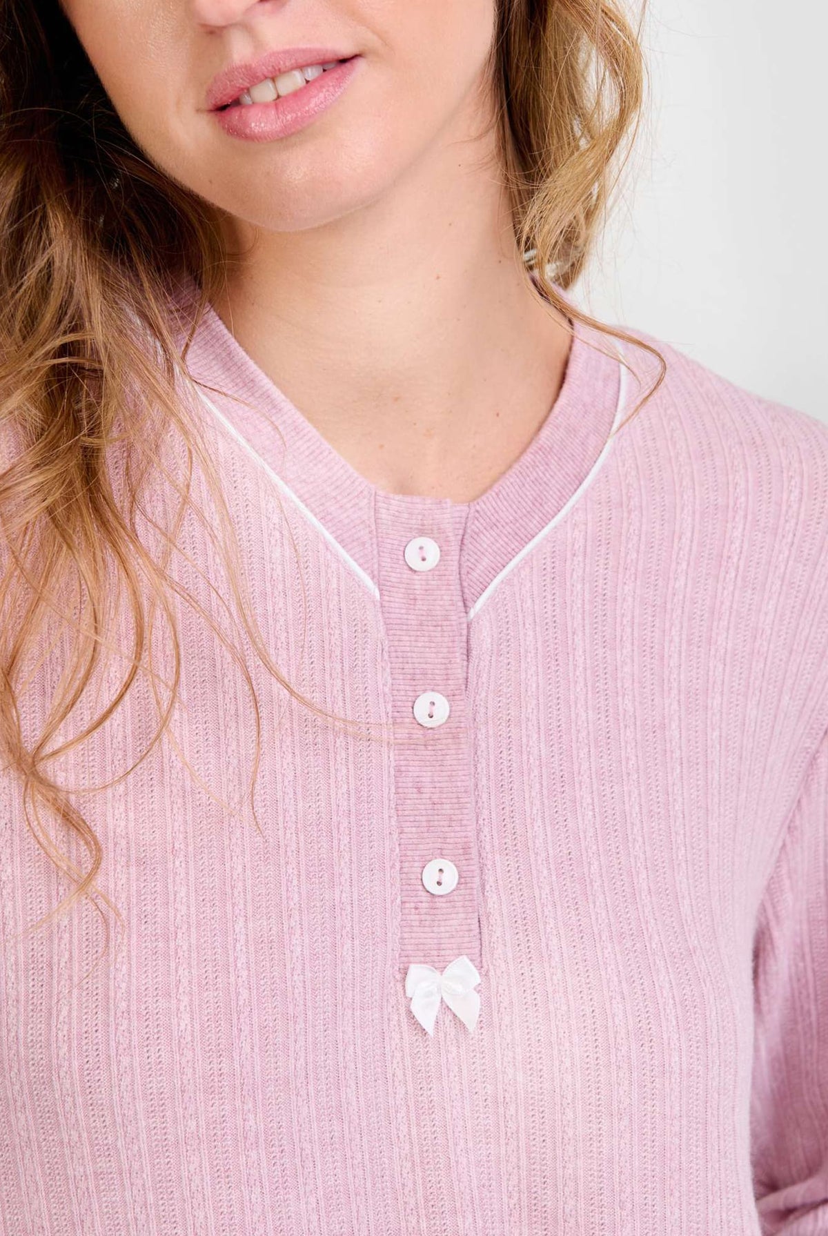 Mujer luce chaquetilla de pijama de invierno rosa de manga larga, cuello con botones blancos y lazo