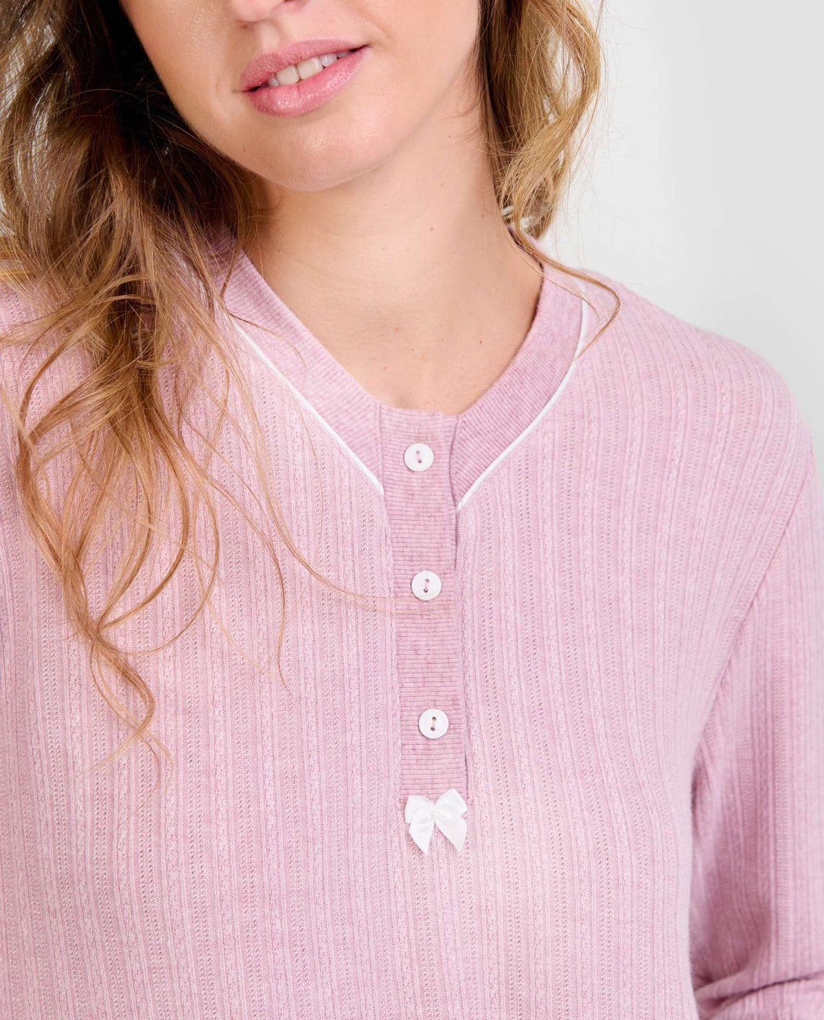 Mujer luce chaquetilla de pijama de invierno rosa de manga larga, cuello con botones blancos y lazo