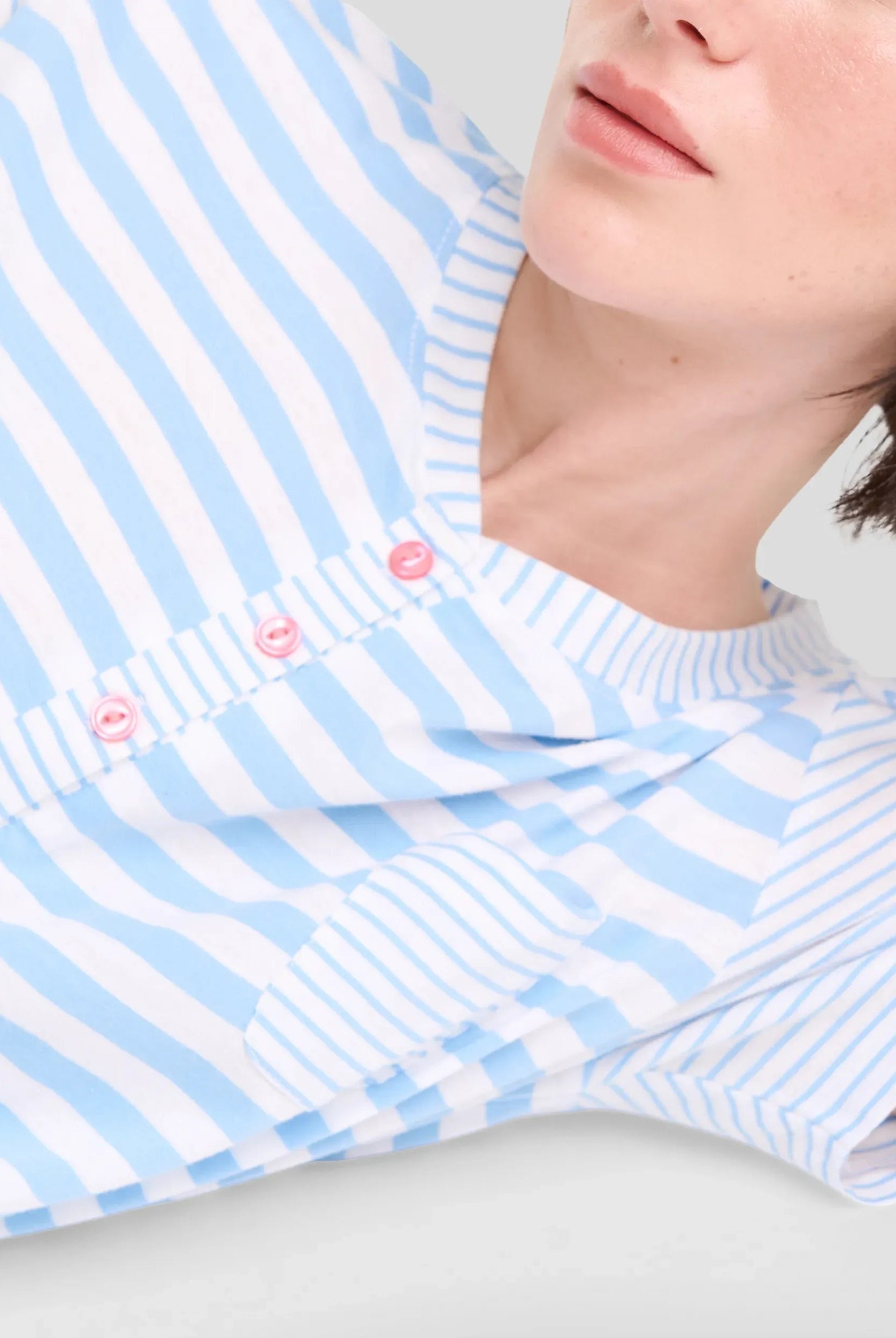 Vista detalle de mujer con camiseta de manga corta a rayas para dormir este verano y cuello con botones rosas