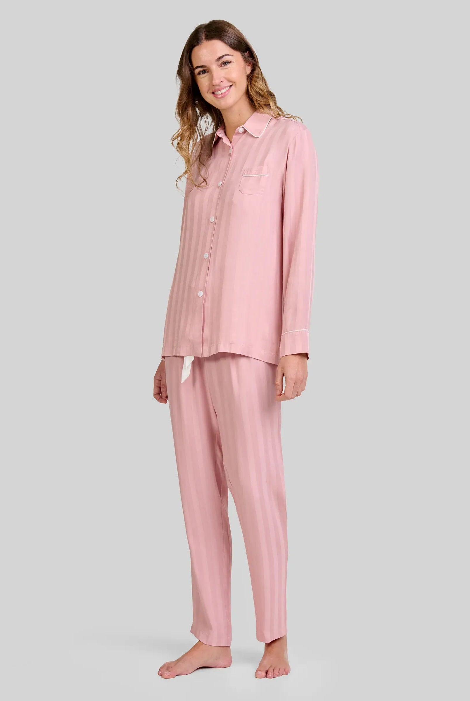 Mujer luce pijama de invierno abierto a rayas rosa palo de manga larga, con botones y bolsillo decorativo
