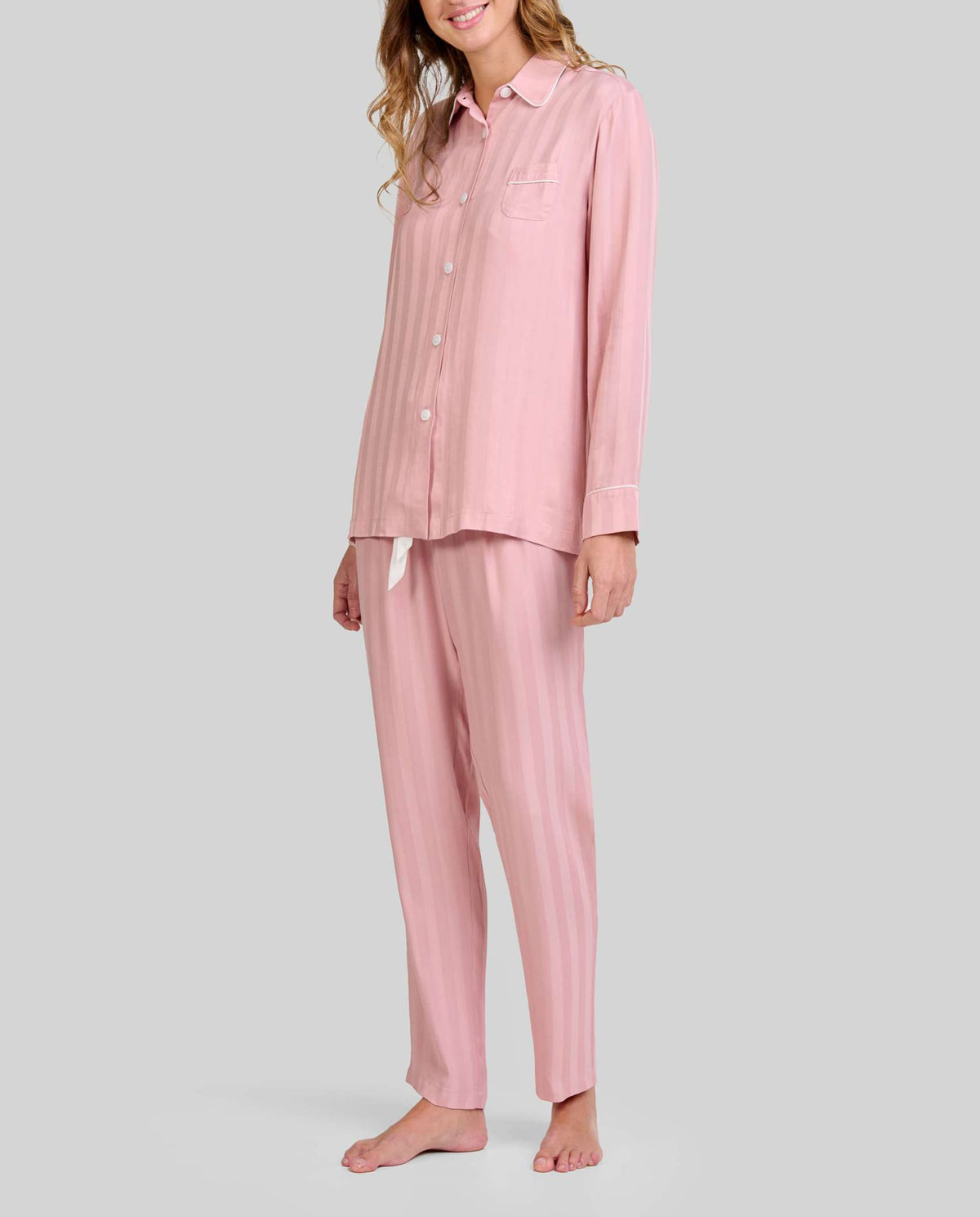 Mujer luce pijama de invierno abierto a rayas rosa palo de manga larga, con botones y bolsillo decorativo