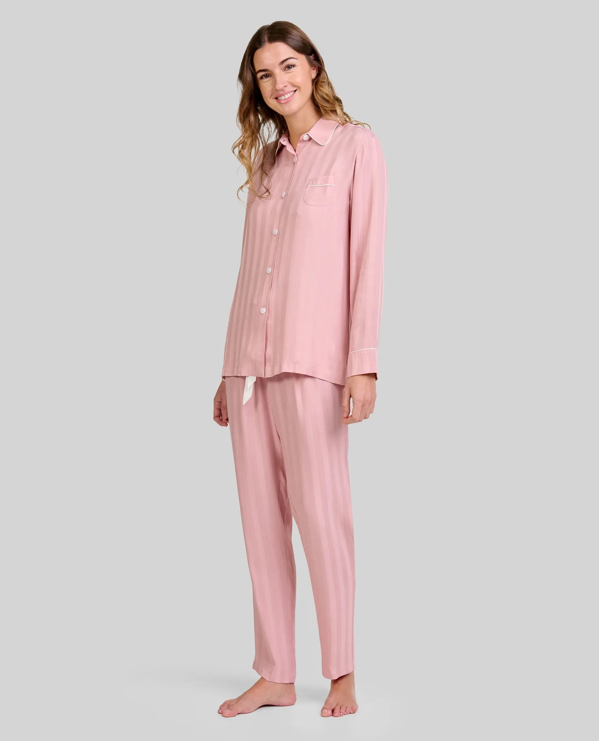 Mujer luce pijama de invierno abierto a rayas rosa palo de manga larga, con botones y bolsillo decorativo