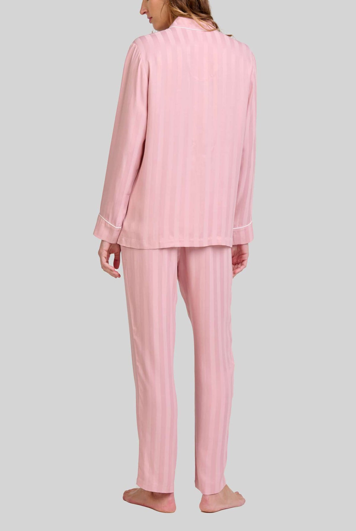 Mujer de espaldas luce pijama rosa palo con rayas verticales y manga larga con detalle vivo en puños