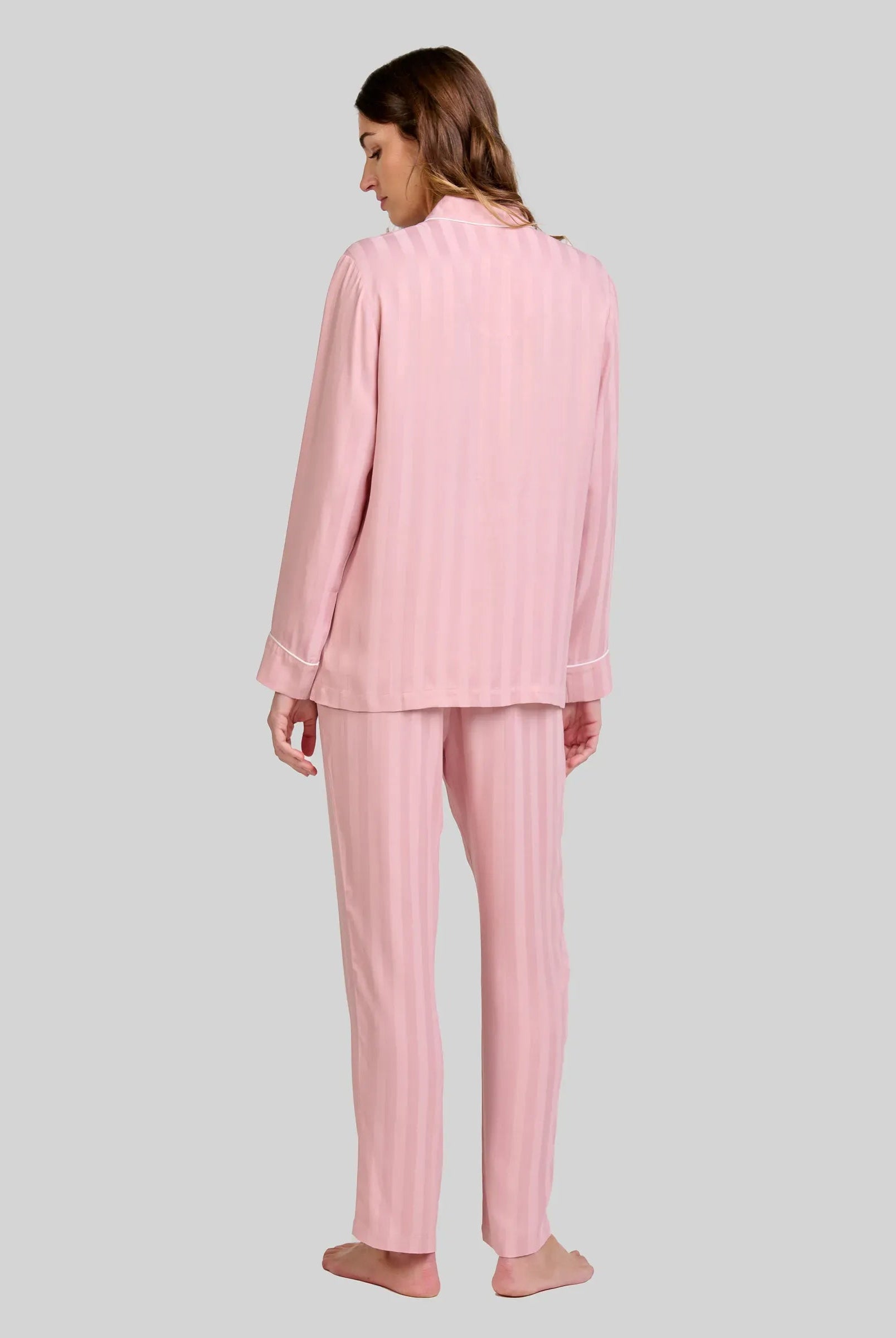 Mujer de espaldas luce pijama rosa palo con rayas verticales y manga larga con detalle vivo en puños