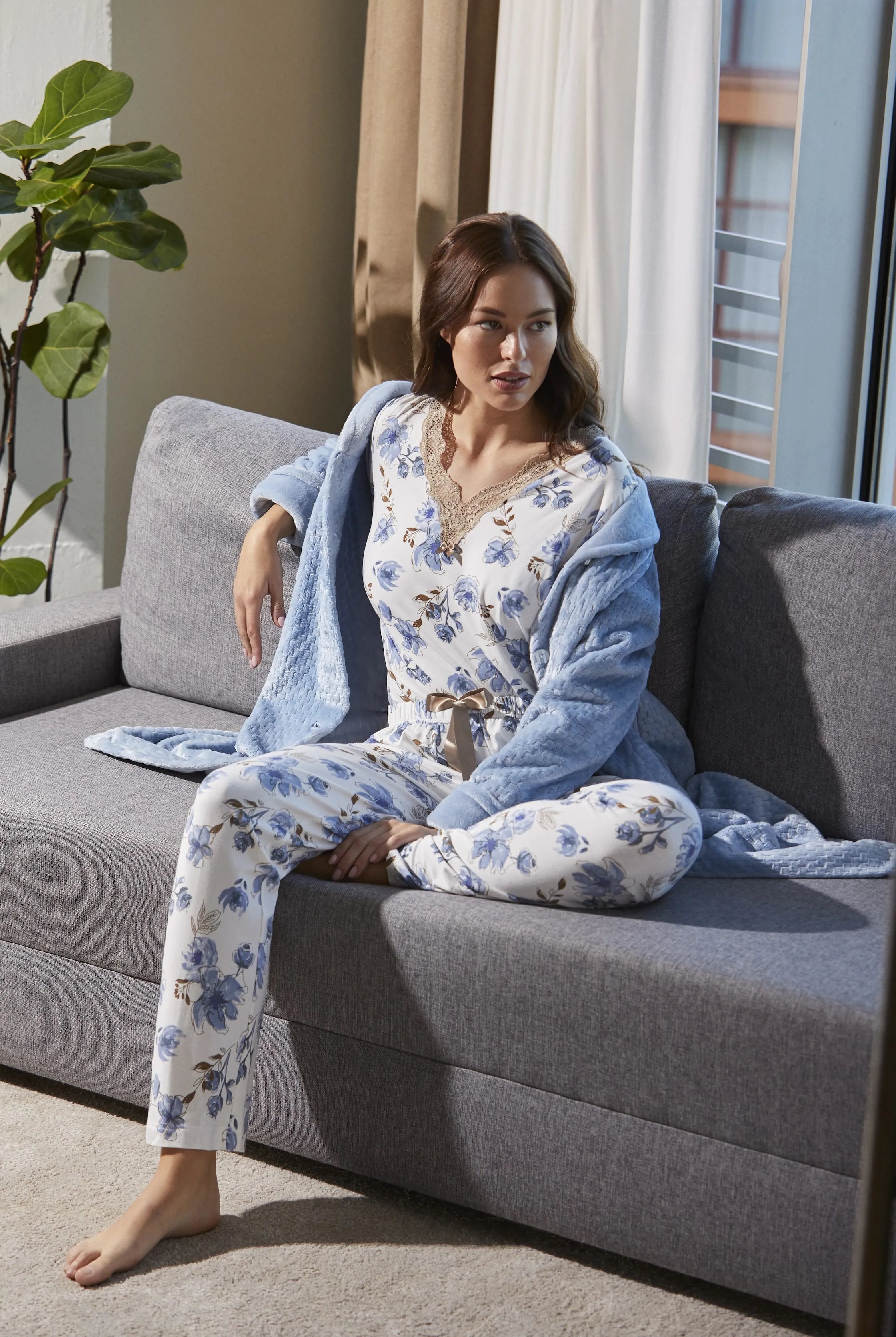 Mujer con pijama floral y bata azul sentada en sofá gris