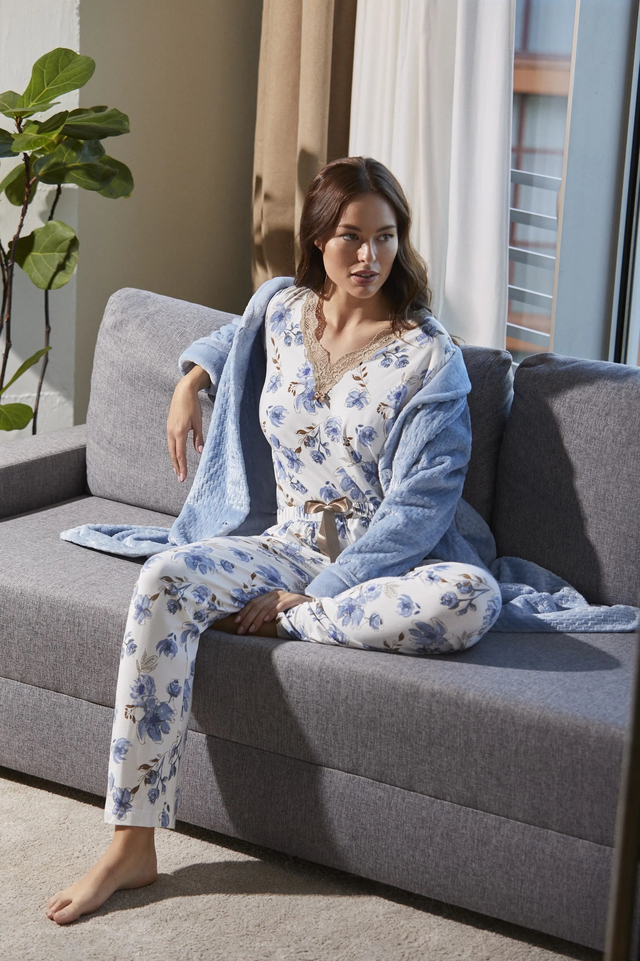 Mujer con pijama floral y bata azul sentada en sofá gris
