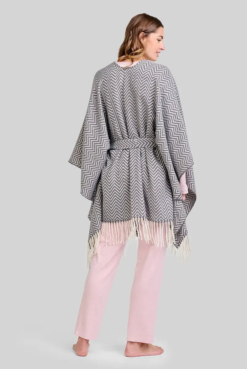 Mujer de espaldas con poncho gris de zigzag y flecos, sobre pijama rosa de invierno