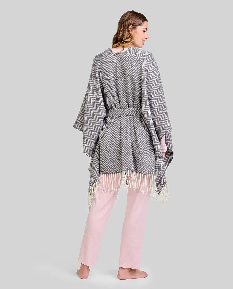 Mujer de espaldas con poncho gris de zigzag y flecos, sobre pijama rosa de invierno