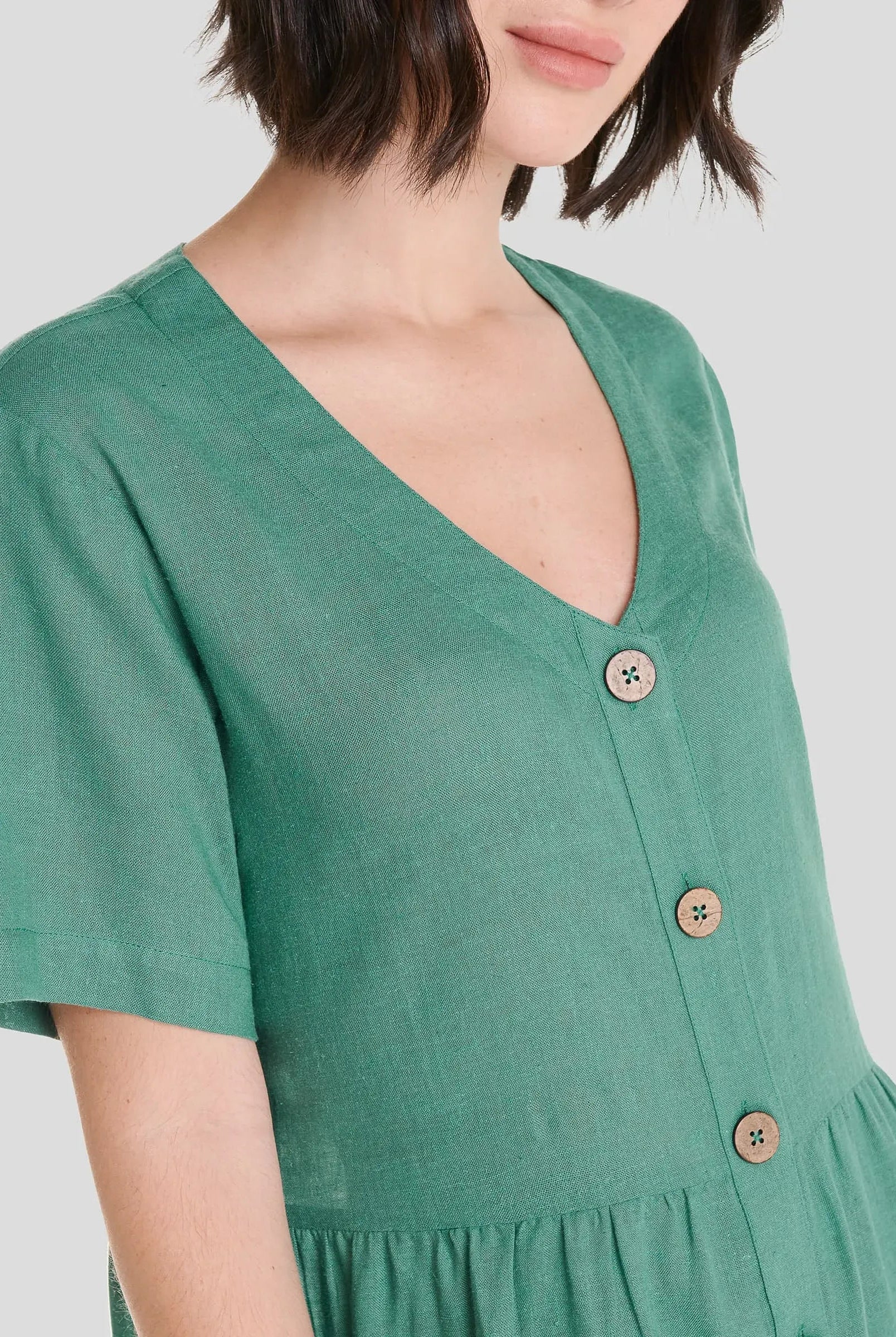 Detalle del escote en pico sin cuello, abotonado del vestido corto de lino verde de verano marca LOHE