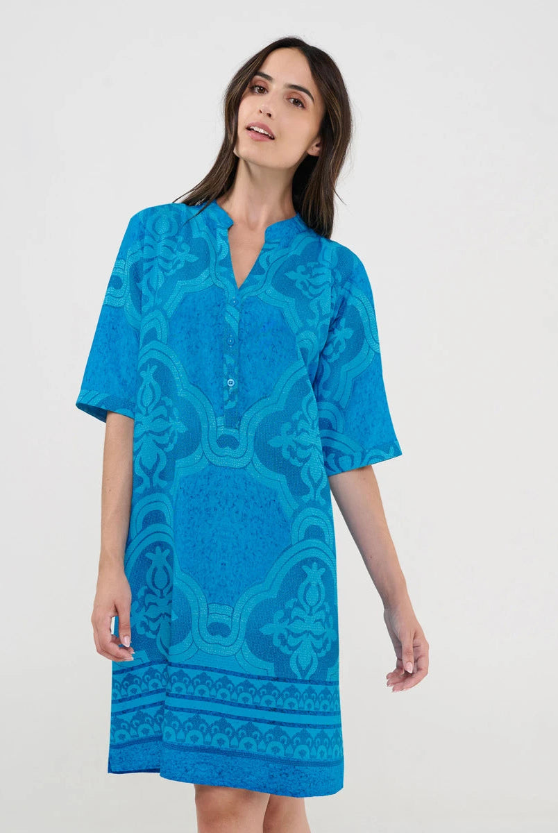 Mujer luciendo vestido turquesa de manga corta con bordados geométricos intrincados y cuello abierto con pata y botones