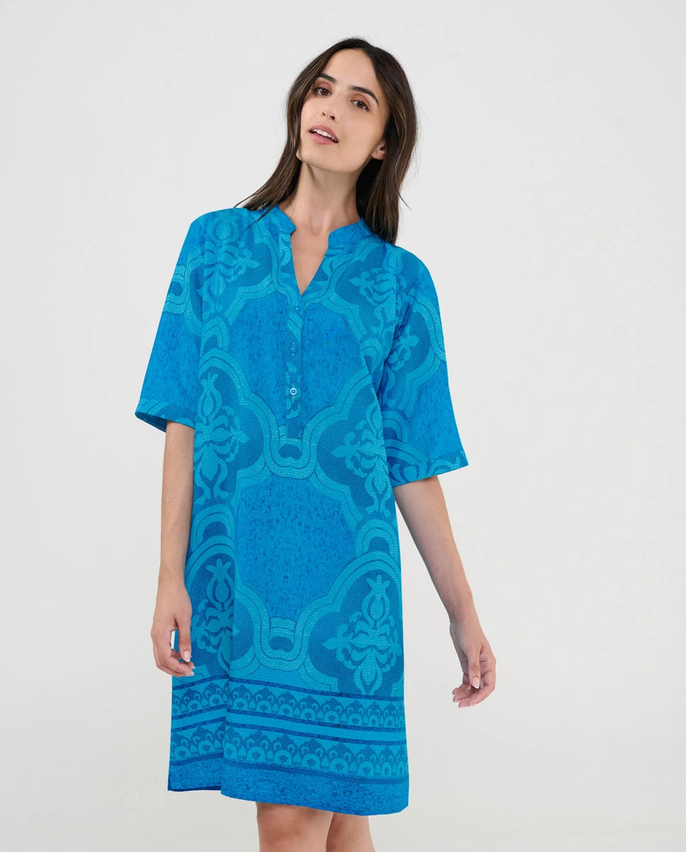 Mujer luciendo vestido turquesa de manga corta con bordados geométricos intrincados y cuello abierto con pata y botones