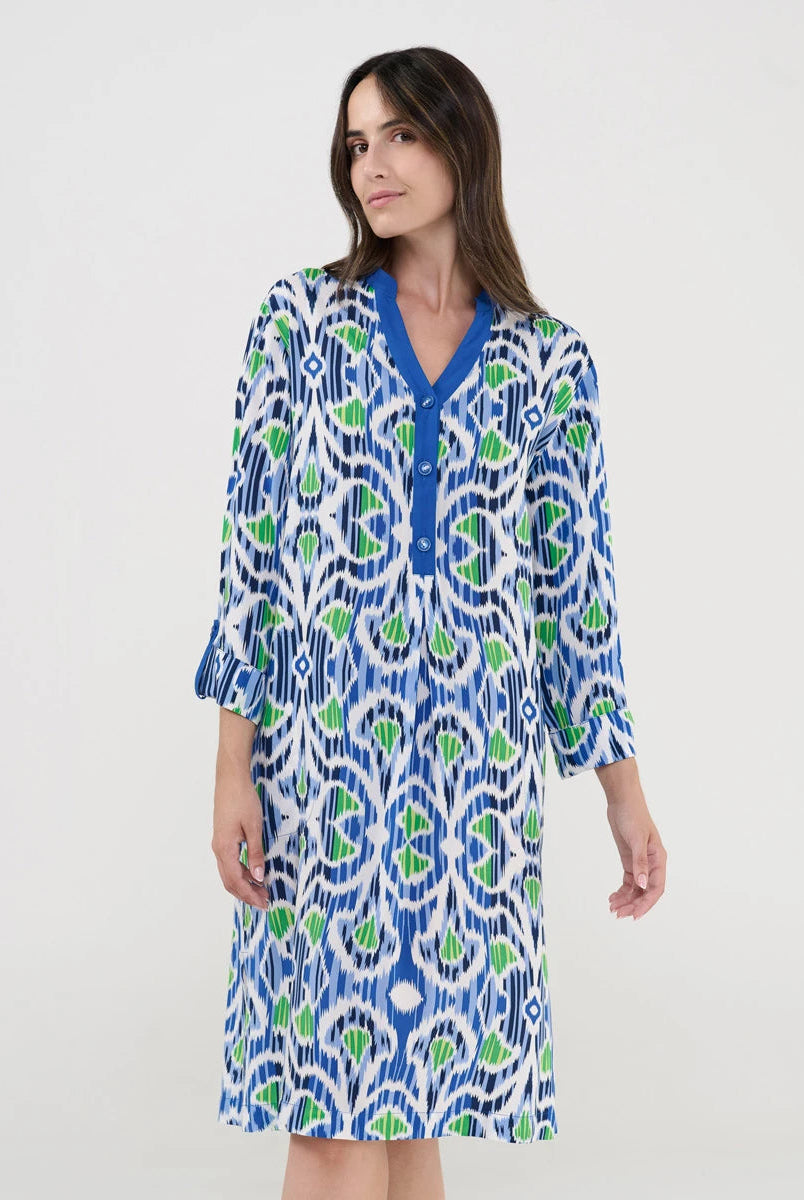 Mujer con vestido estampado azul y verde caminando junto a una piscina al aire libre.