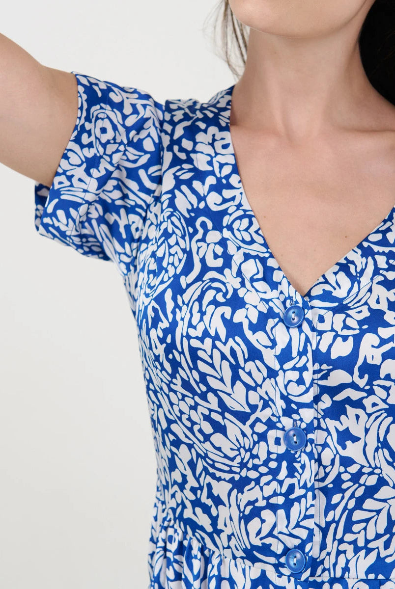 Detalle del torso de una mujer con vestido veraniego azul y blanco estampado, escote en V y botones frontales.