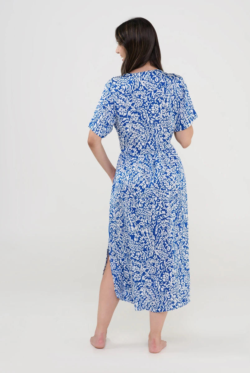 Vista trasera de una mujer con vestido midi azul estampado en blanco y abertura lateral.