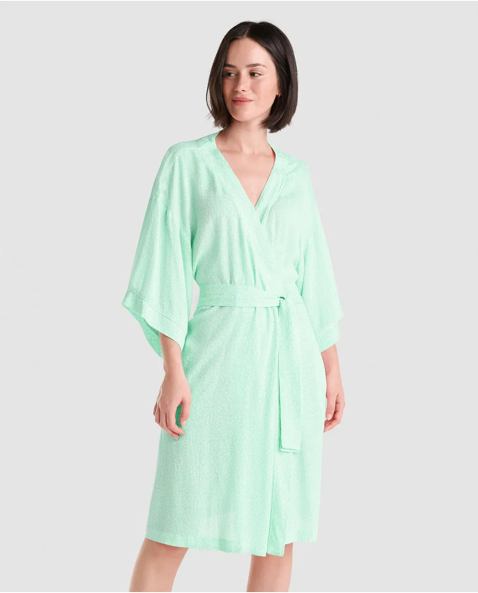 Woman in green viscose summer short dressing gown with polka dot print, side pockets, belt and French sleeves.