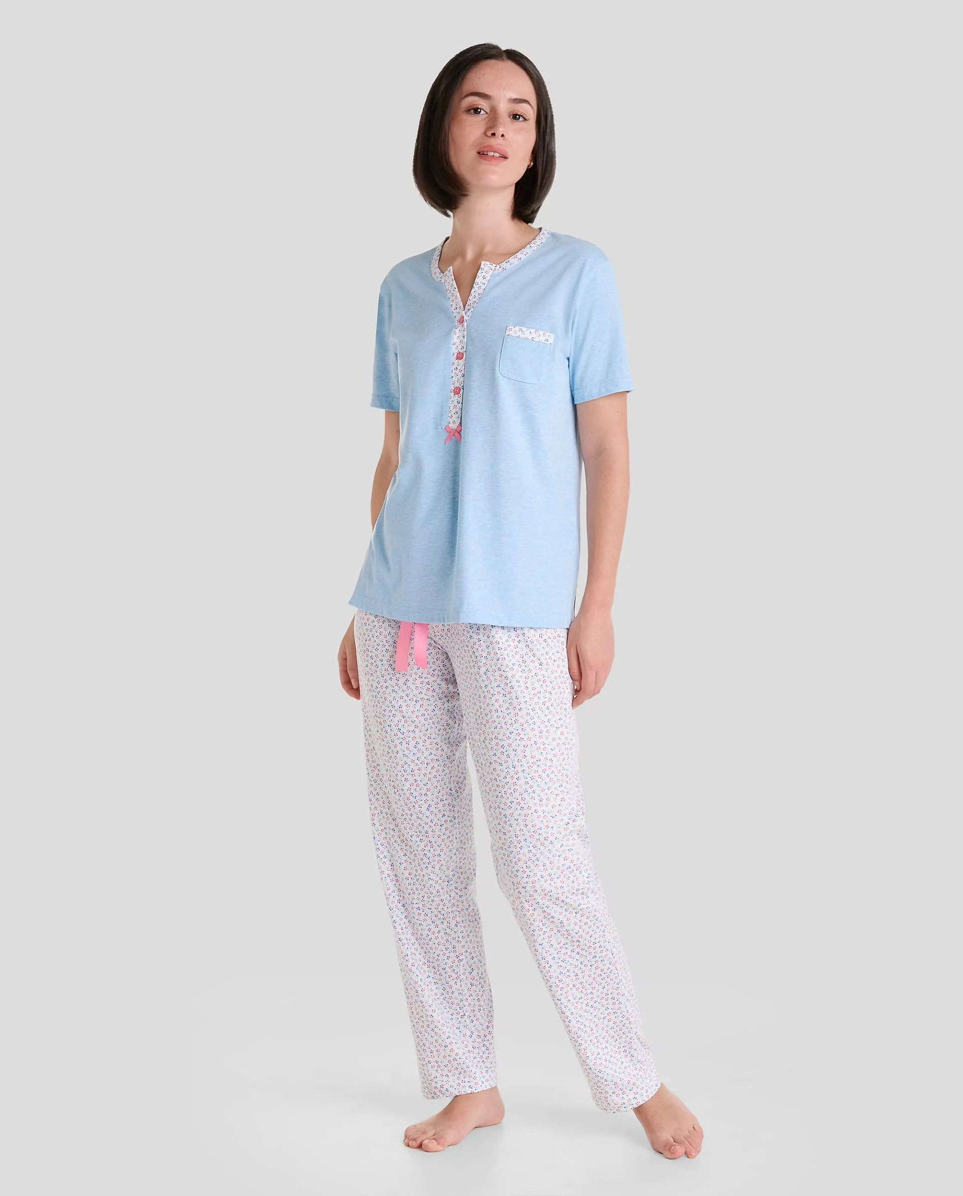 Woman wears short-sleeved light blue pyjama top and floral pyjama trousers with pink satin bow.