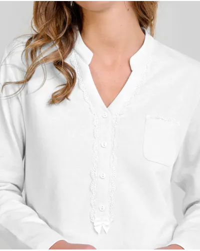 Woman wearing ivory-coloured long nightdress pyjamas with an open neckline, lace trim and bow