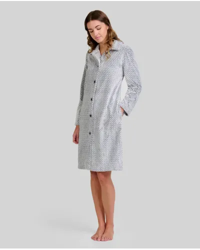 Woman standing barefoot wearing a long light grey herringbone robe with buttons down the front and her hands in her pockets.
