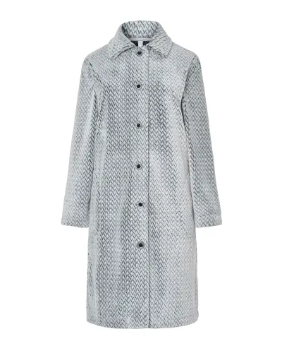 Woman standing barefoot wearing a long light grey herringbone robe with buttons down the front and her hands in her pockets.