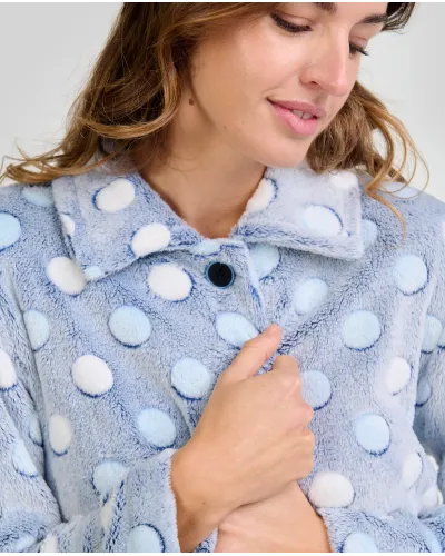 Mujer en bata celeste de lunares en relieve hasta la rodilla, manga larga y botones con bolsillos laterales.