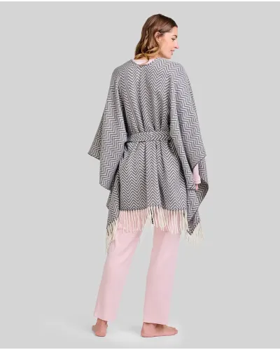 Woman wearing light pink pyjamas and a grey poncho with fringes and a belt