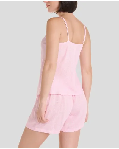 Woman wearing a pink summer pyjama set with straps, lace-up neckline and shorts. White polka dot print.