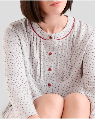 Woman wearing a long winter nightdress with a floral print, pleats and red detailing.