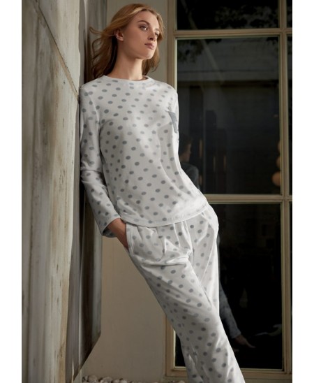 Model poses by window in long-sleeved pyjamas with silver polka dot round neck.