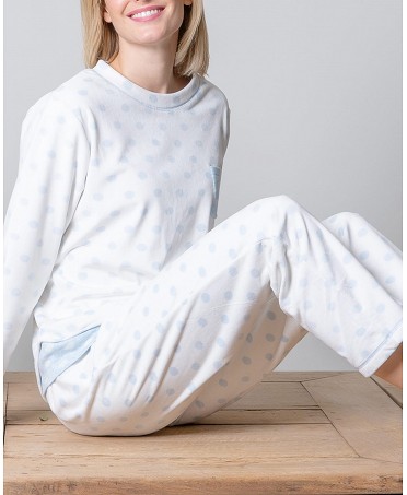 Woman in long blue polka-dotted pyjamas sitting at wooden table.