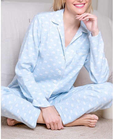 A comfortable woman sits on the floor wearing blue polka-dotted winter pyjamas.