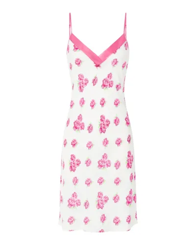 A woman wearing a short white nightgown with straps and a V-neck with a fuchsia flower print.
