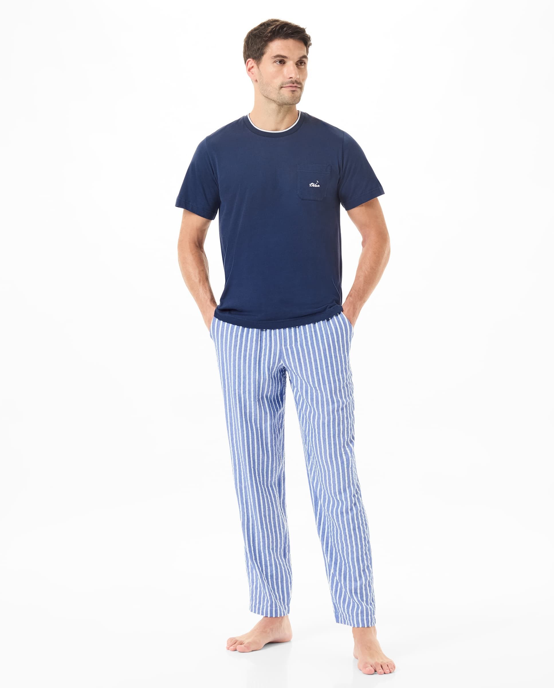 Un hombre vistiendo pijama con pantalón a rayas y una camiseta azul marino.