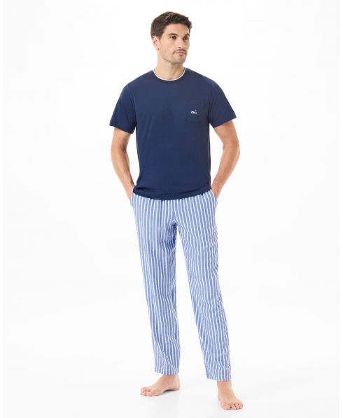 Un hombre vistiendo pijama con pantalón a rayas y una camiseta azul marino.