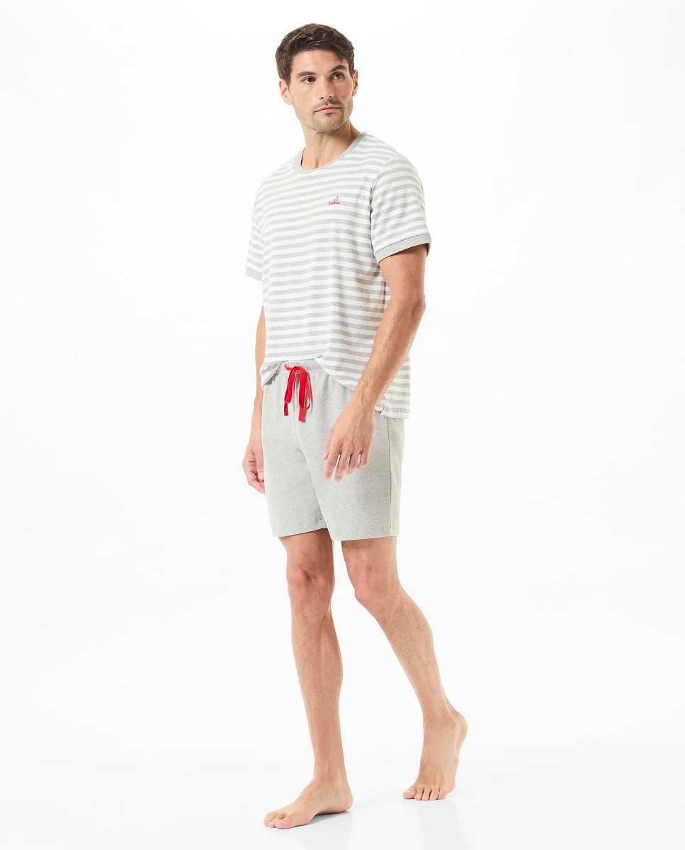 A man wears a grey striped pyjama top and summer shorts.